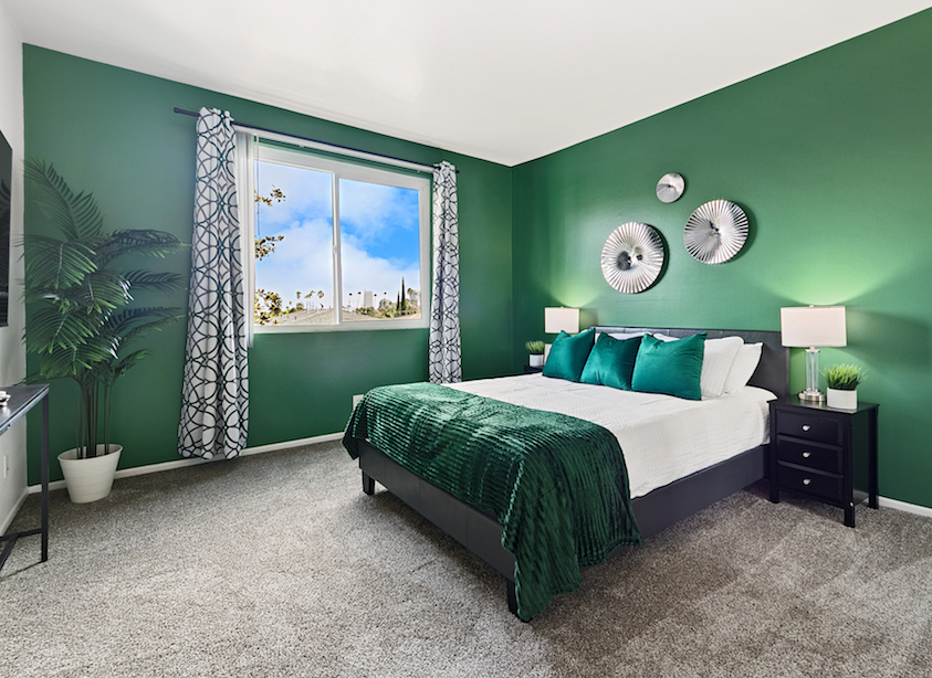 Primary bedroom with emerald walls, teal bedding, and patterned curtains