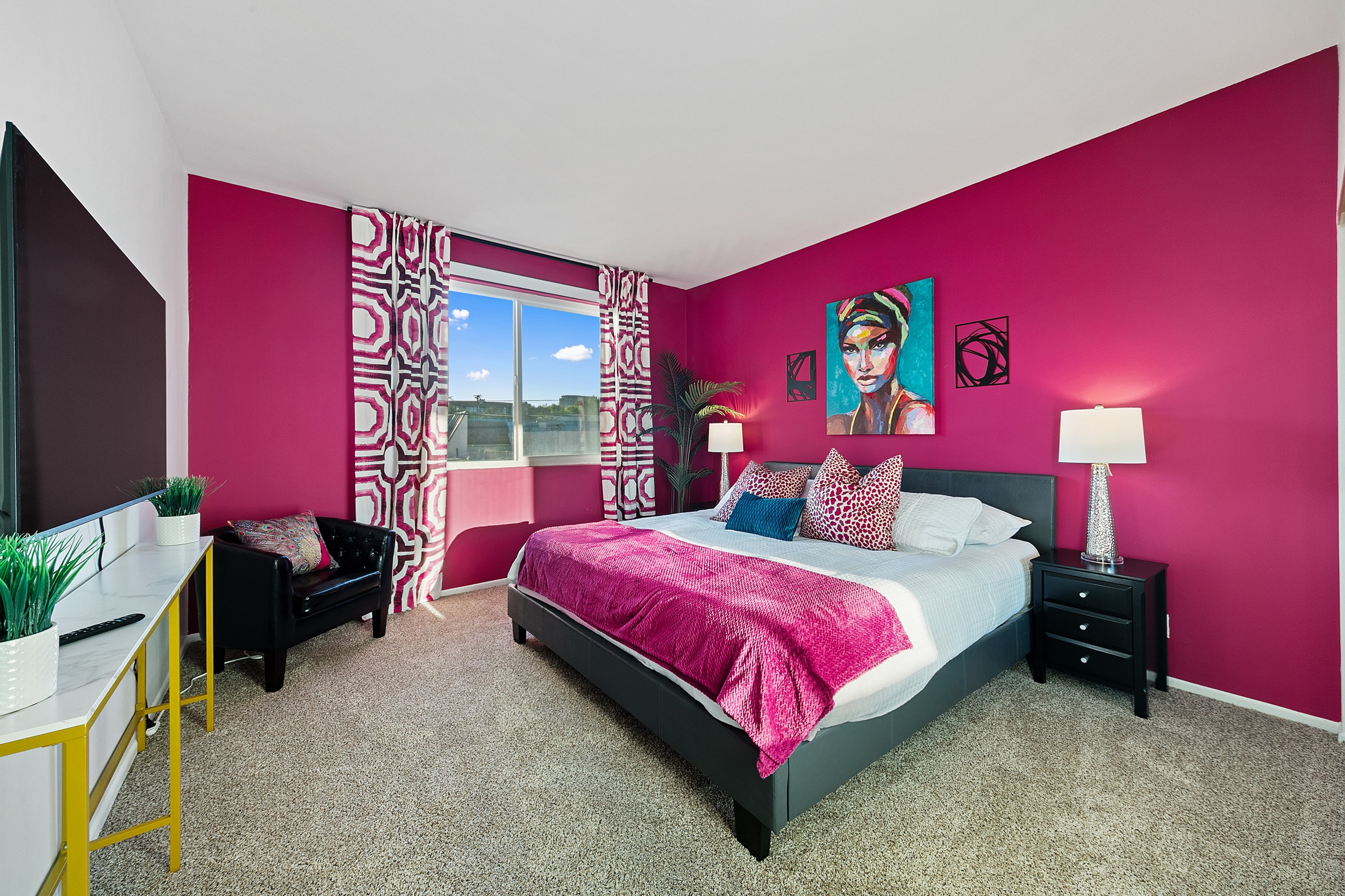 Fuchsia bedroom with patterned curtains, black furniture, and colorful artwork
