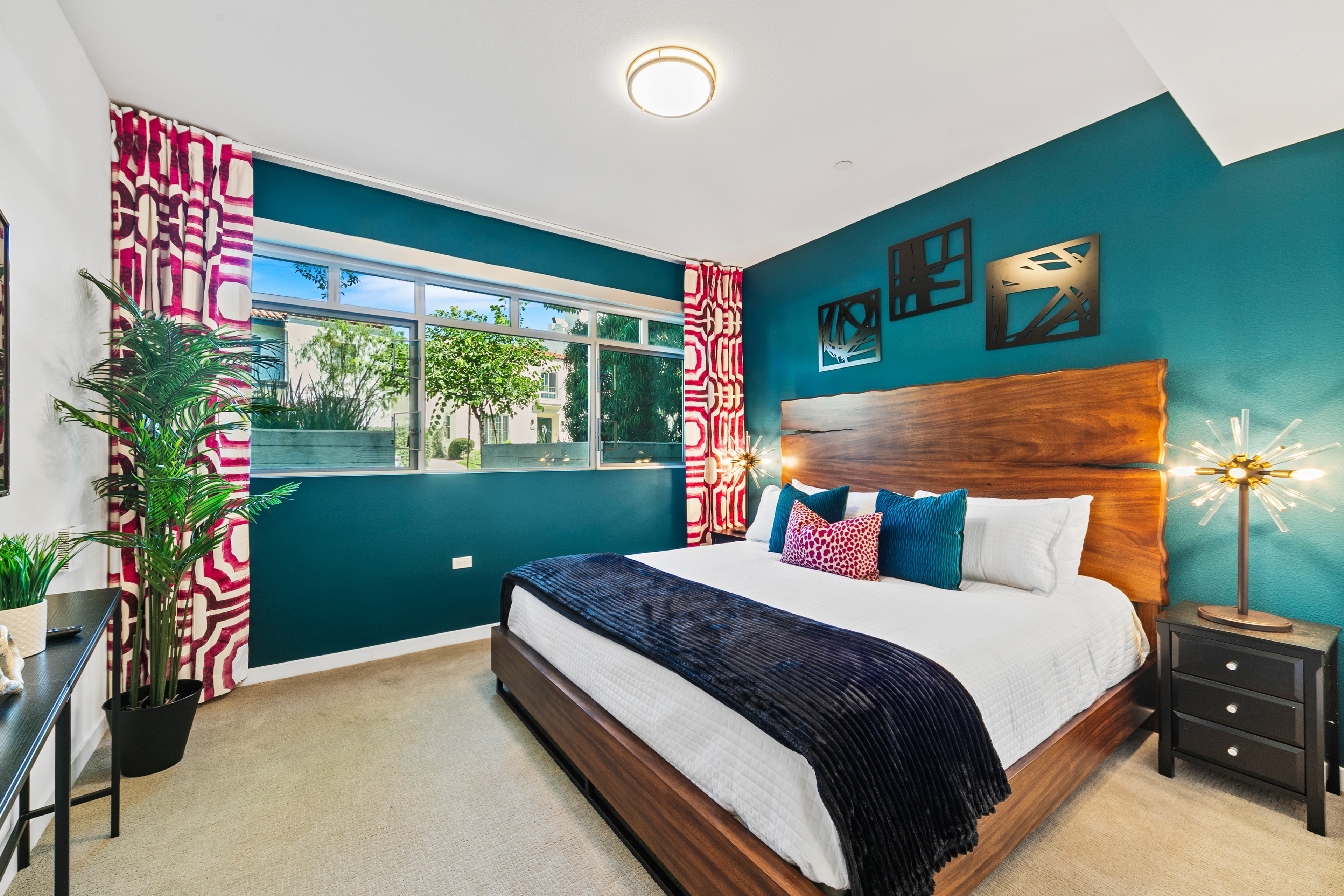 Teal bedroom with a sculptural wood headboard and fuchsia patterned curtains
