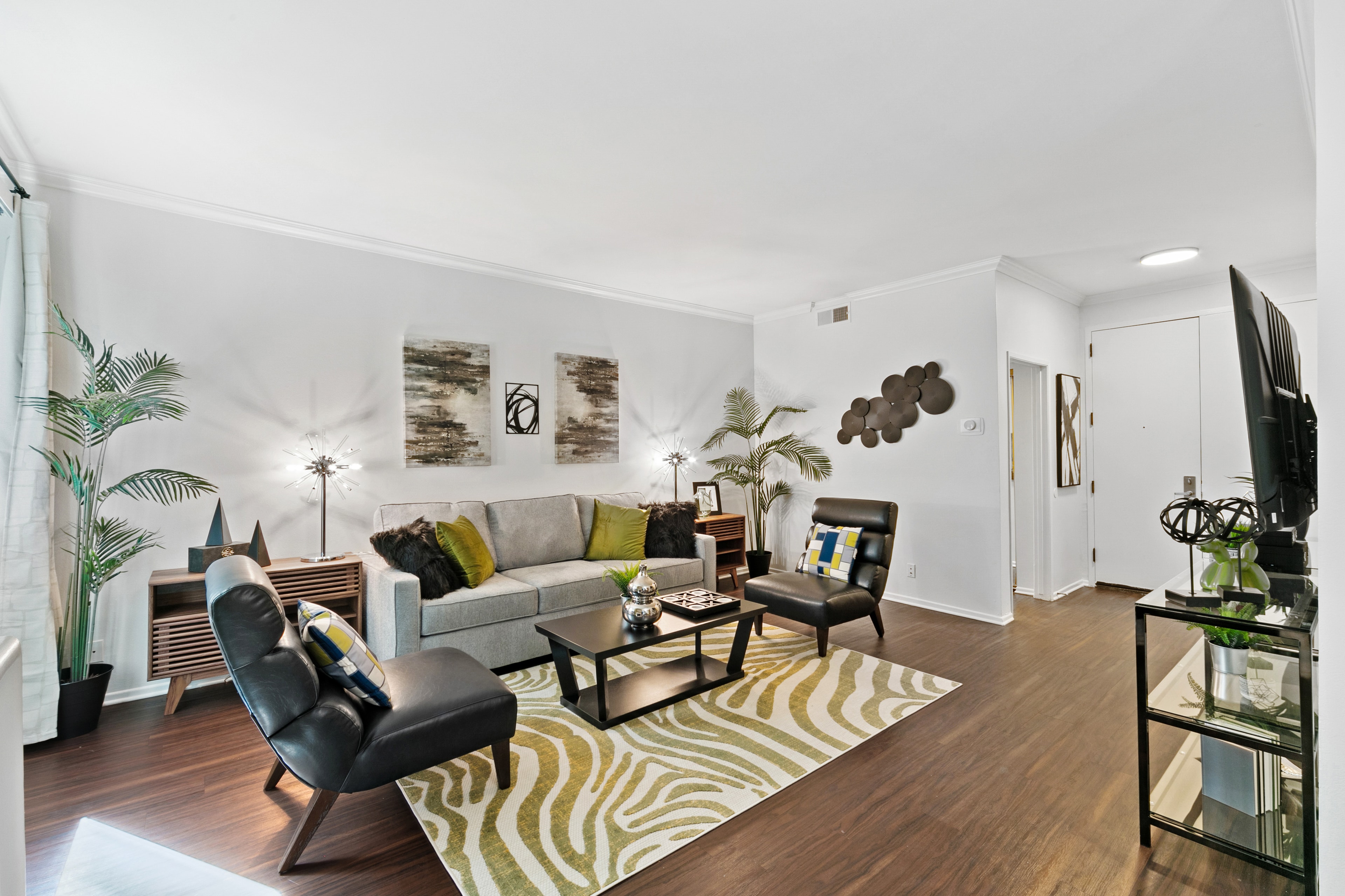Living room with green accent pillows, dark wood flooring, and sculptural decor