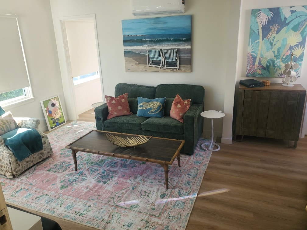 Living room with deep green sofa, coastal artwork, and patterned rug