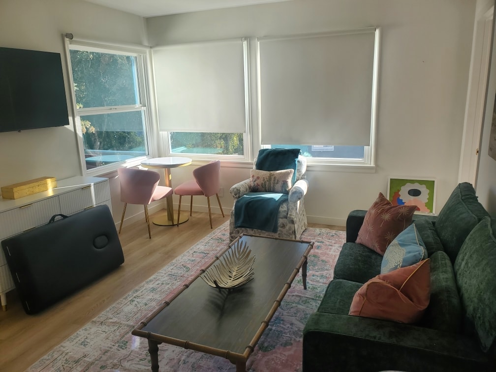 Bright sitting room with green sofa, pink chairs, and large windows