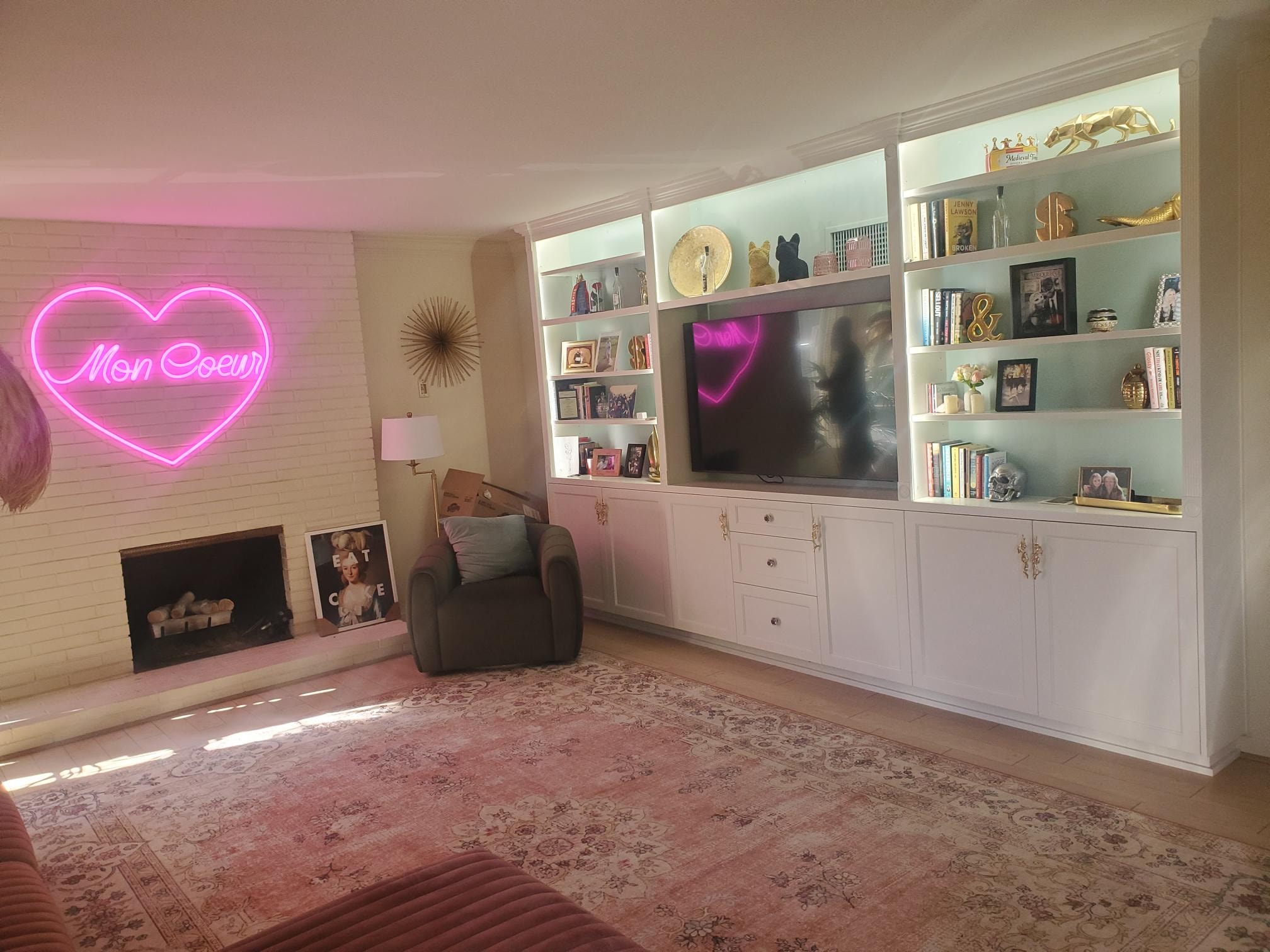 Built-in living room shelving beside a white brick fireplace and pink neon heart