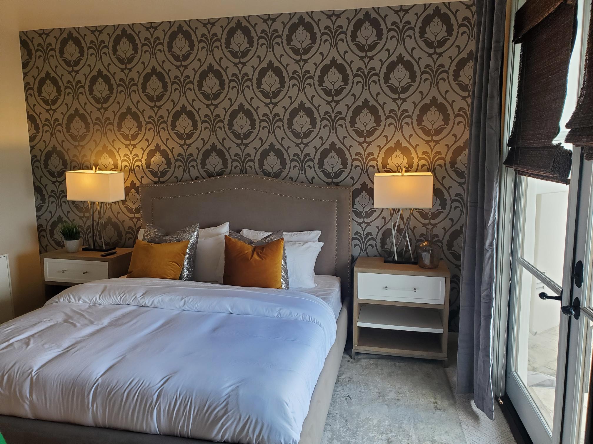 Bedroom with damask wallpaper, upholstered bed, and mustard accent pillows