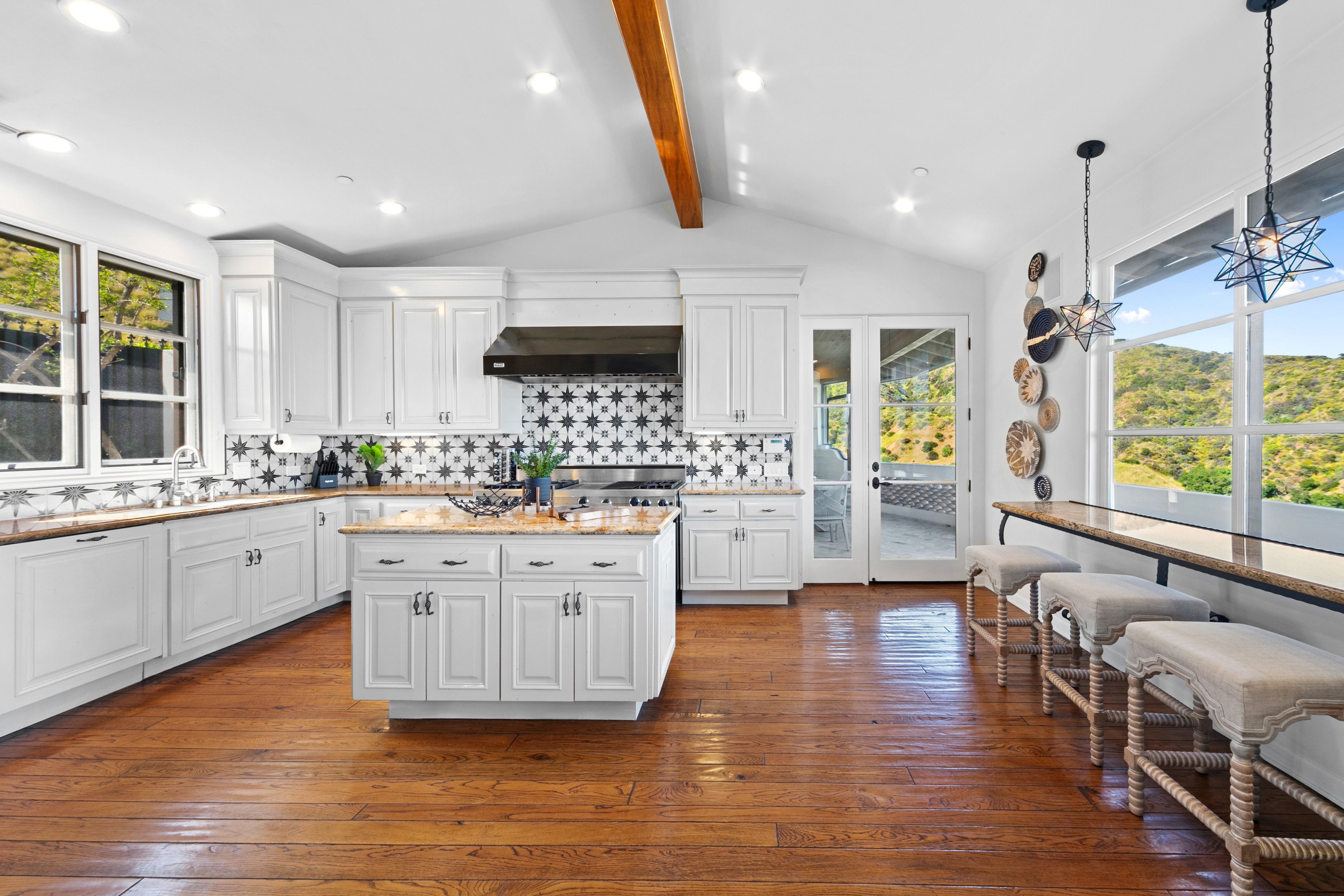 White kitchen with patterned tile backsplash, wood floors, and hillside views
