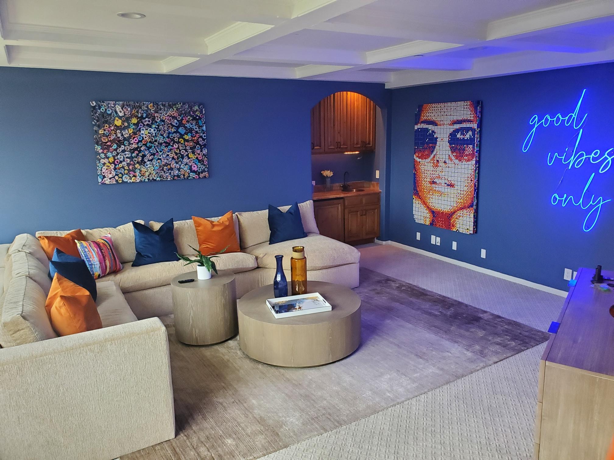 Media room with sectional seating, blue walls, neon sign, and arched bar