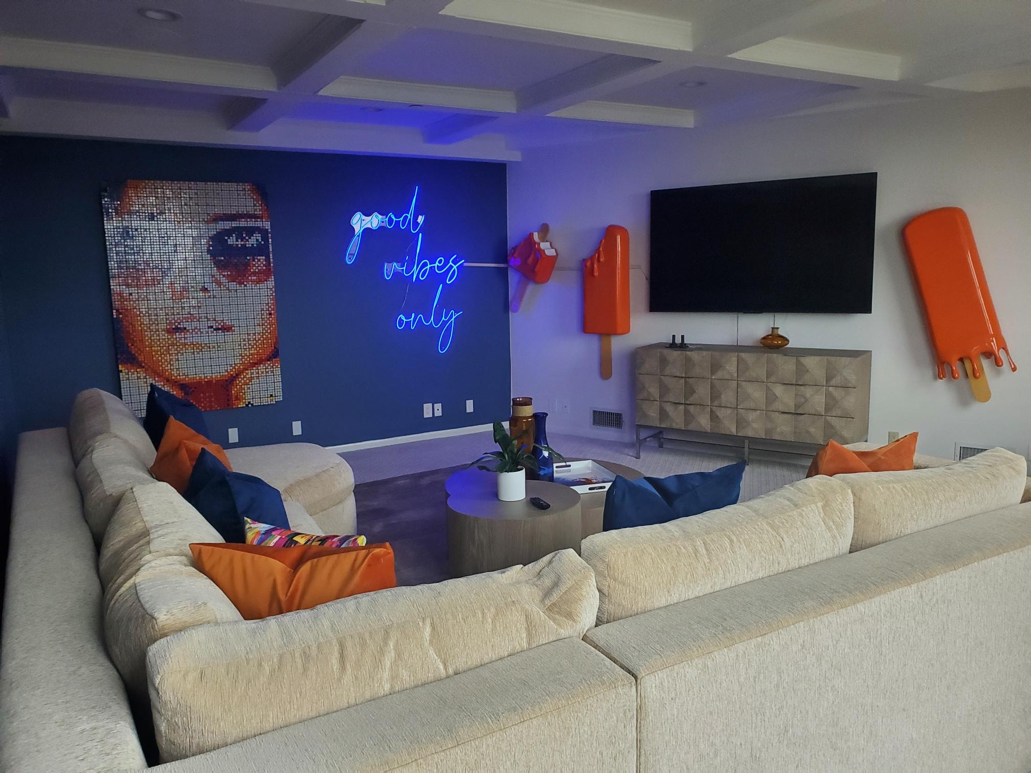 Media room with blue accent wall, neon sign, television, and orange pop-art details