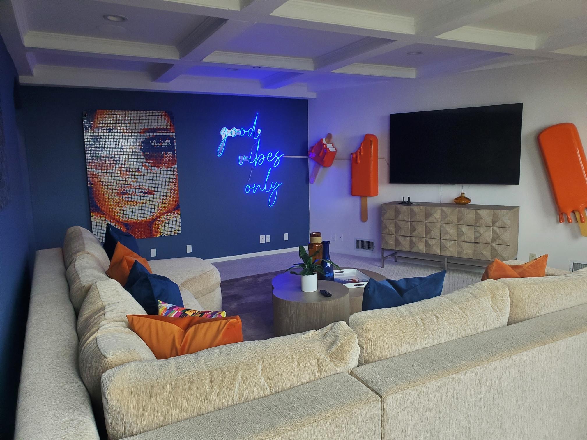 Media room with sectional seating, blue neon sign, and colorful wall art
