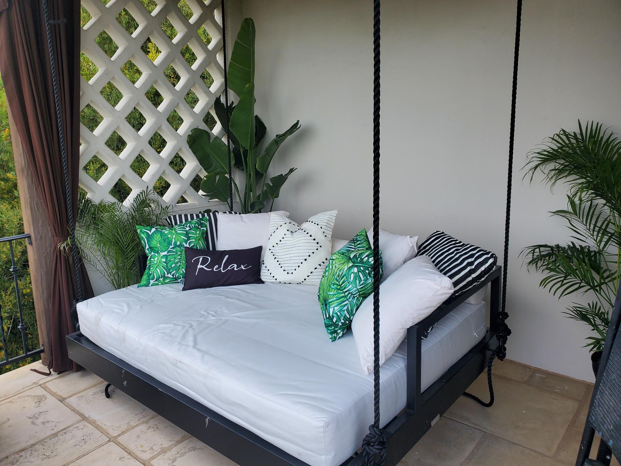 Outdoor swing daybed with tropical pillows and lush greenery