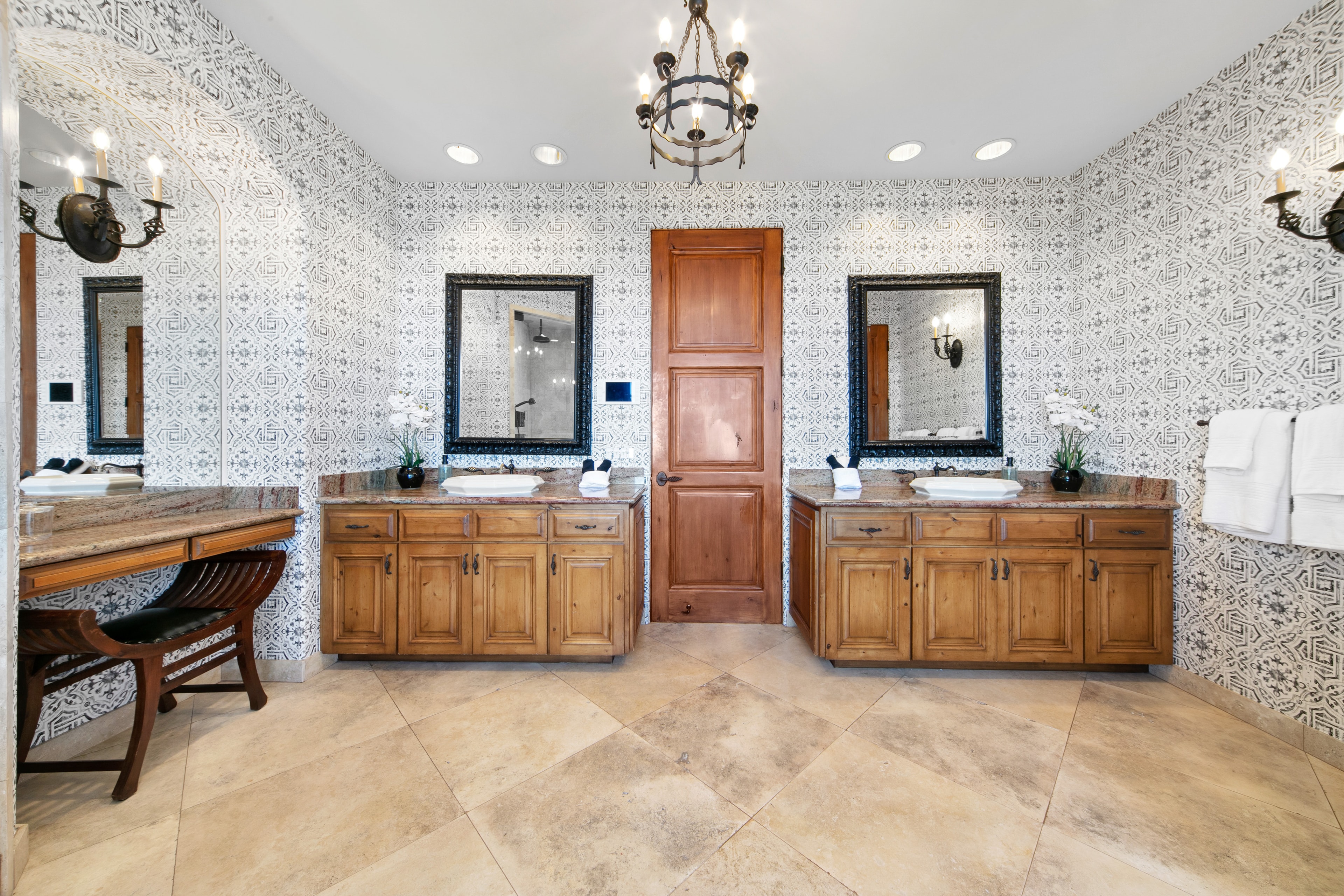 Primary bathroom with patterned wallpaper, wood vanities, and double mirrors