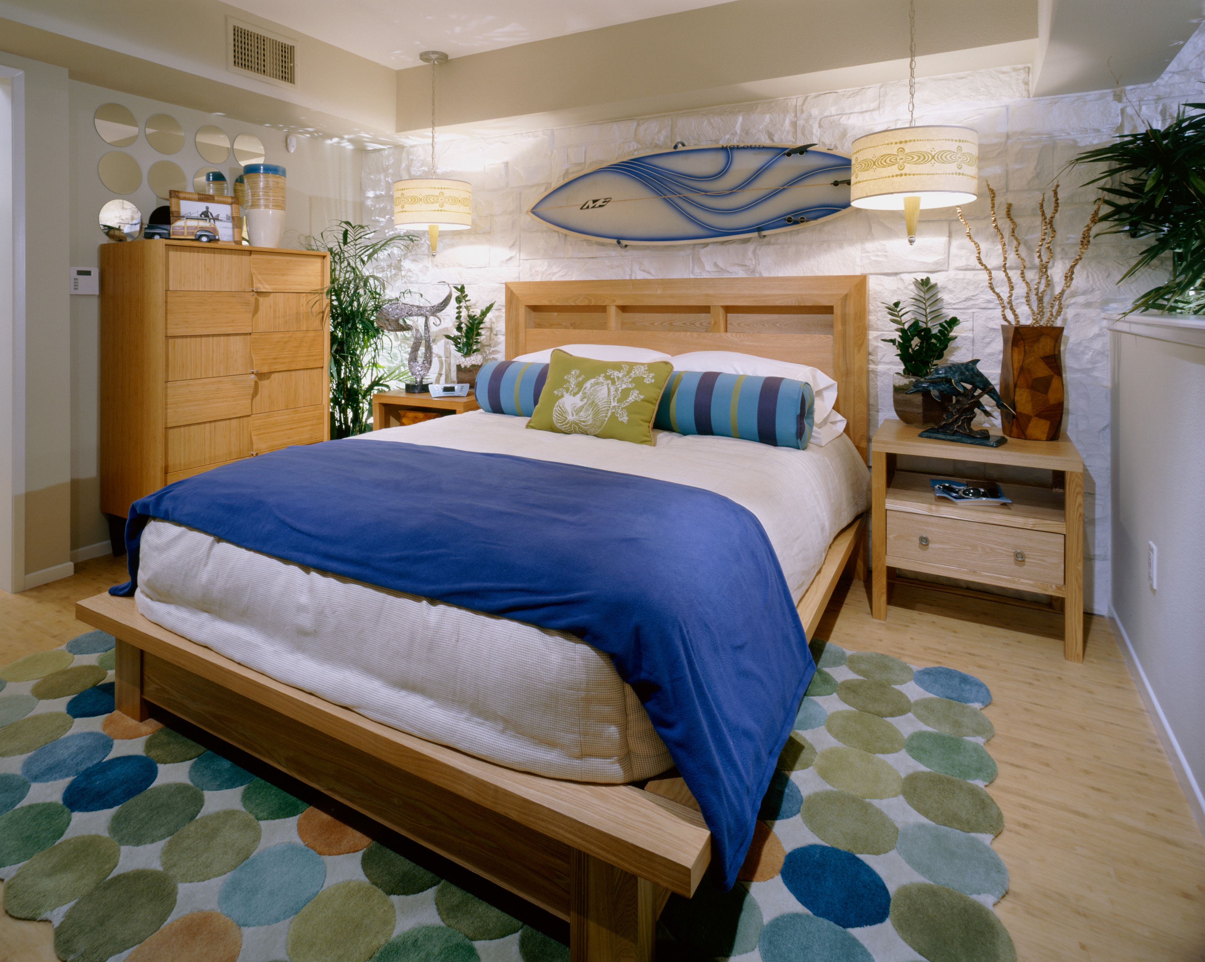 Primary bedroom with a surfboard wall display, blue bedding, and warm wood furniture