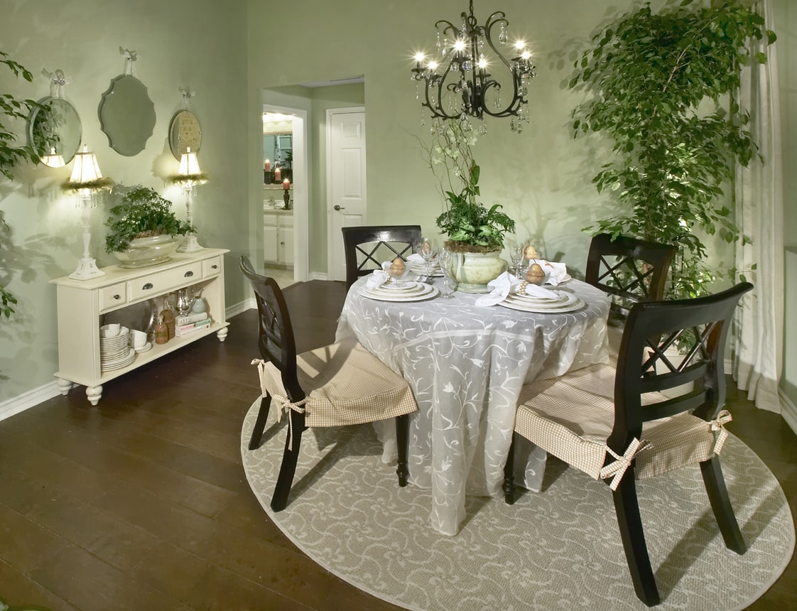 Formal dining room with round table, black chandelier, and lush greenery
