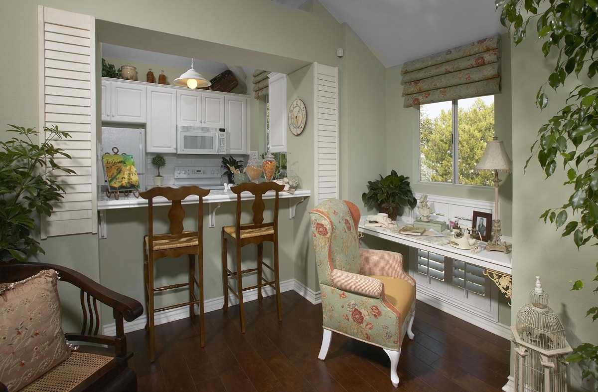 Sage green kitchen and sitting area with floral chair, white cabinetry, and dark wood floors