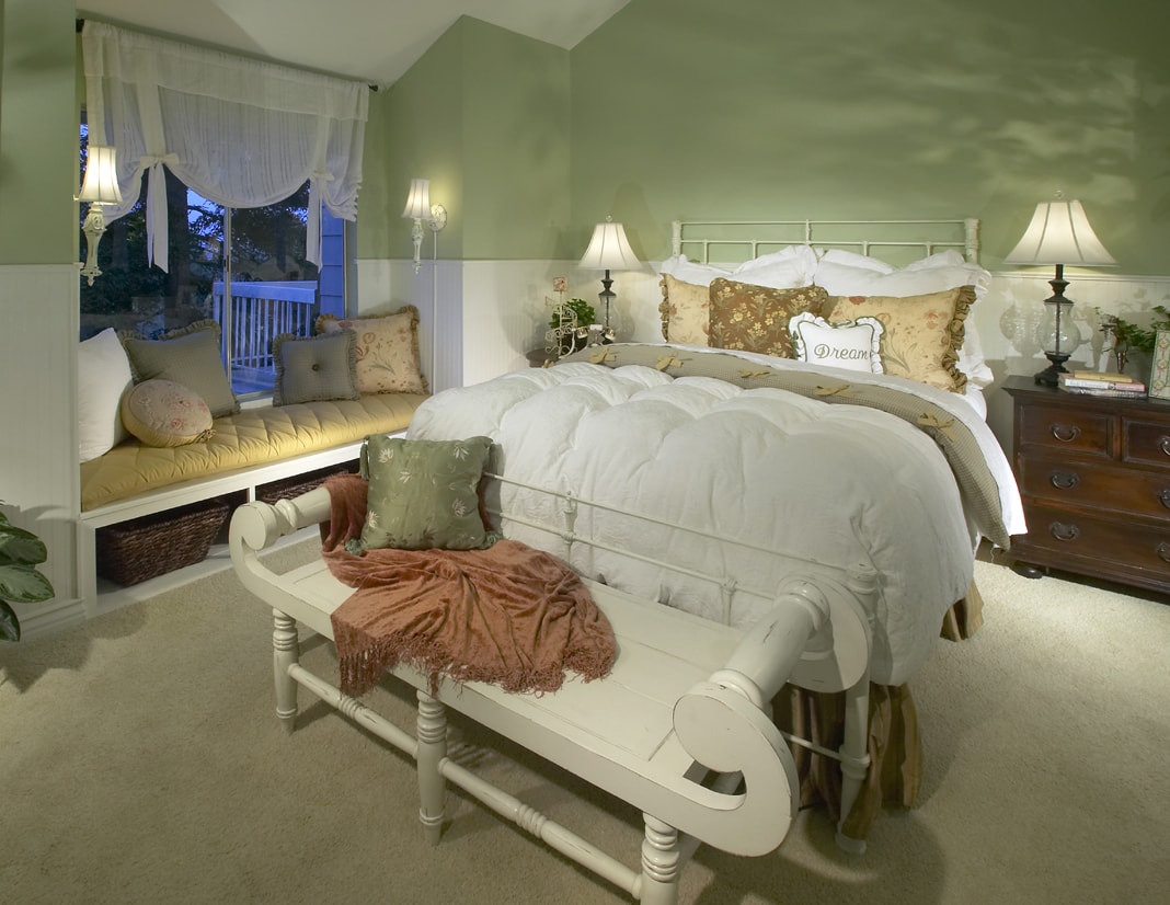 Primary bedroom with white iron bed, window seat, and sage green walls