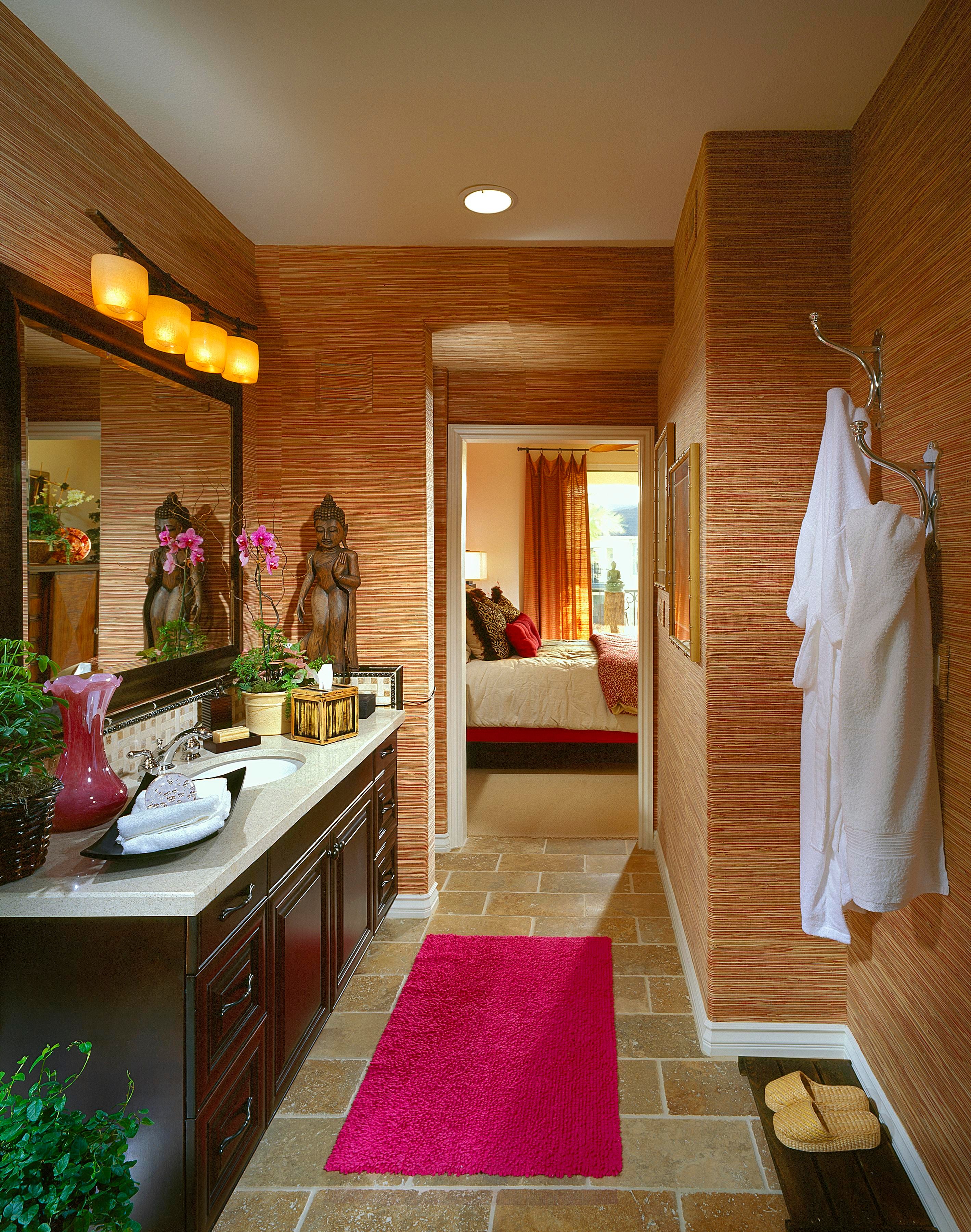 Bamboo-textured bathroom with dark vanity, amber lights, Buddha sculptures, and a magenta runner