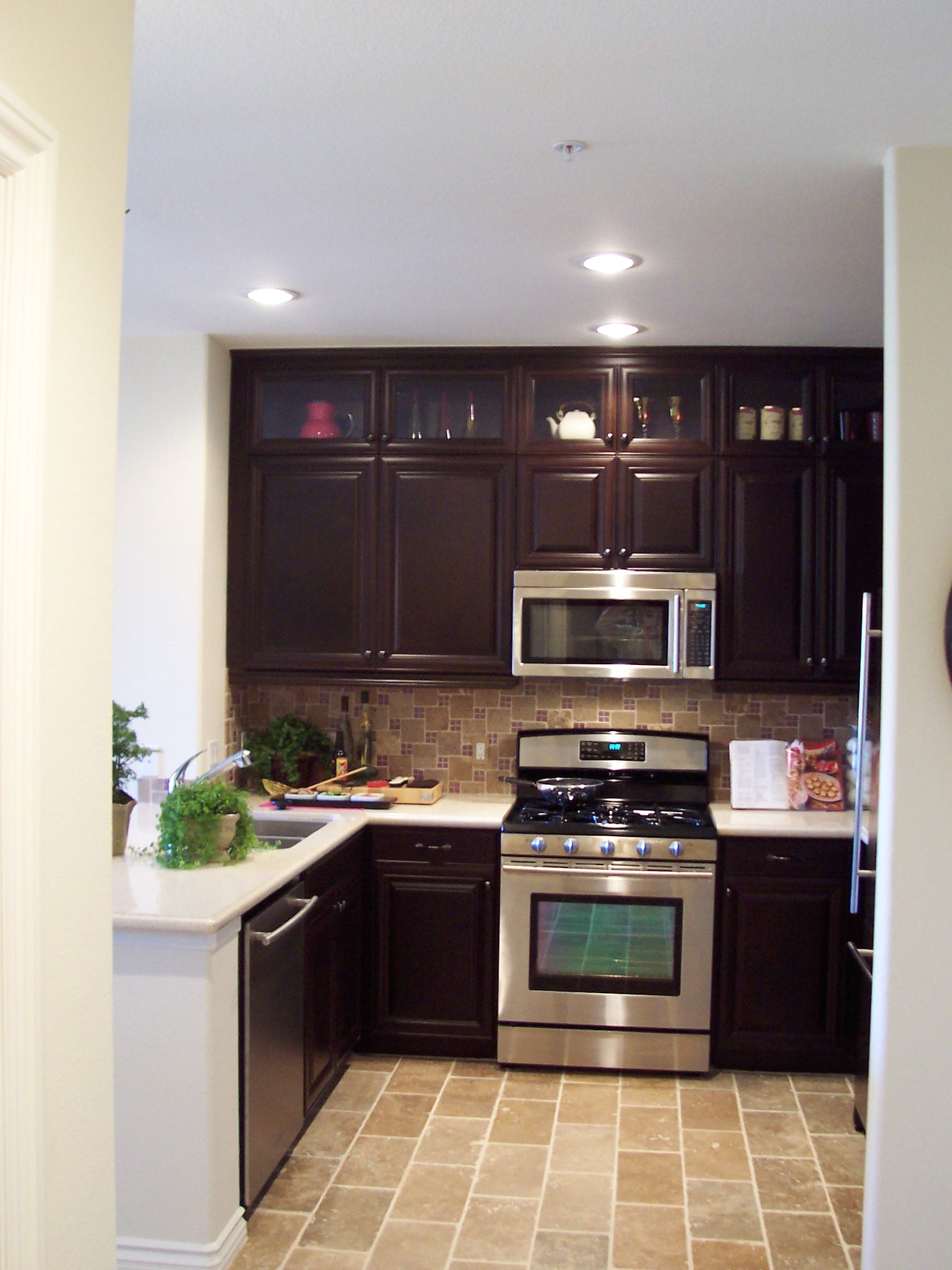 Dark wood kitchen with stainless steel appliances, mosaic backsplash, and stone flooring