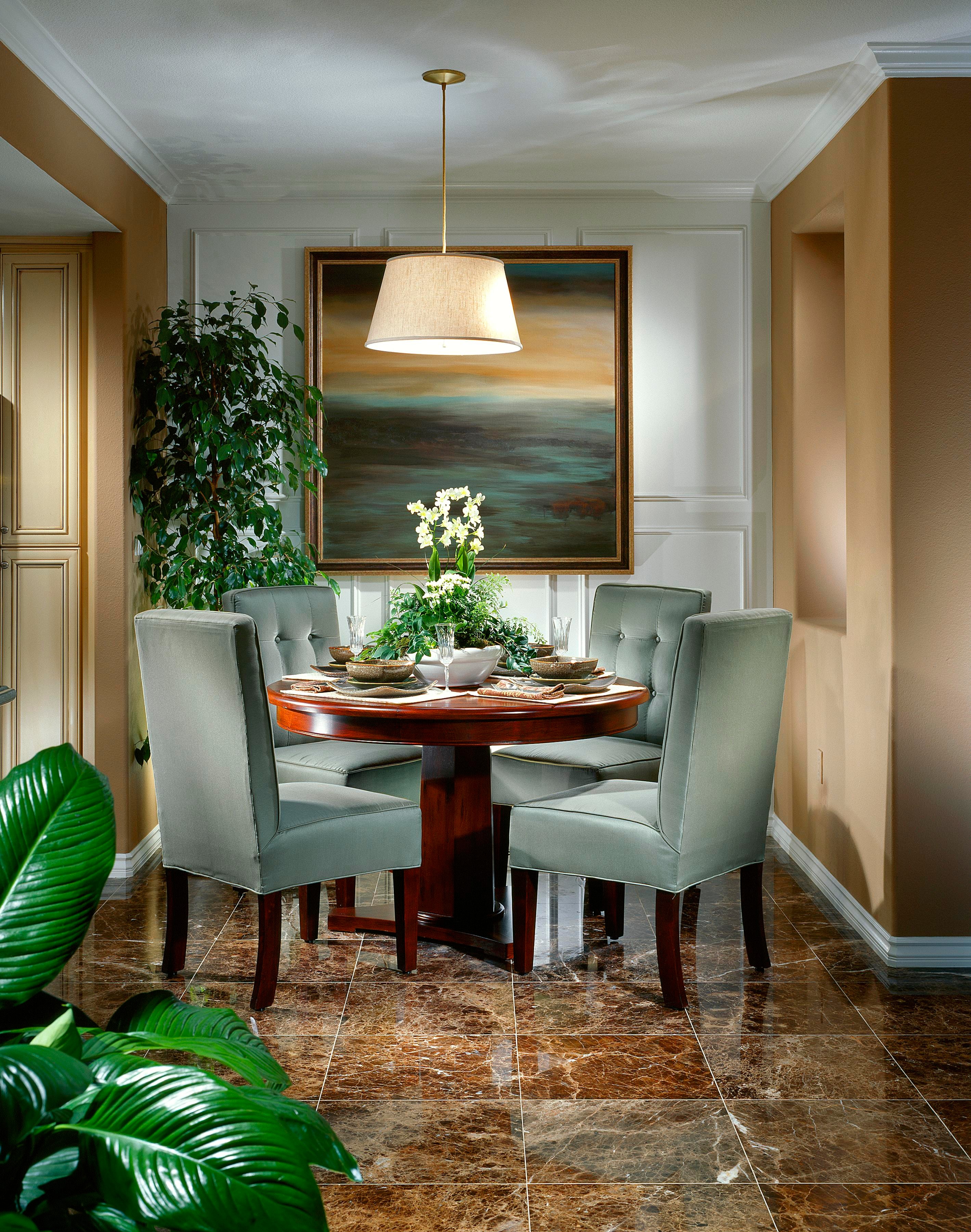 Formal dining room with round wood table, sage upholstered chairs, and statement artwork