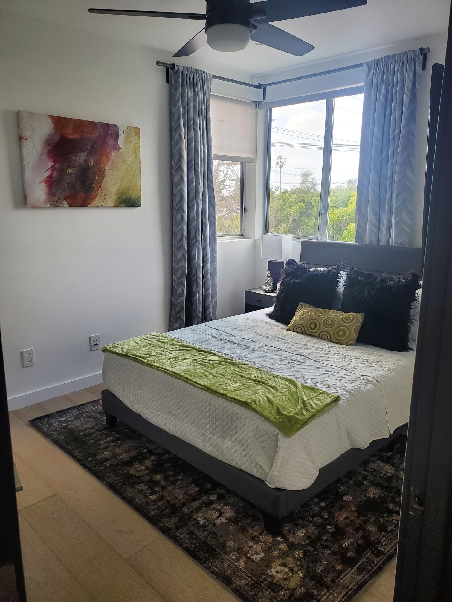 Bedroom with green accent pillows, patterned curtains, and contemporary artwork