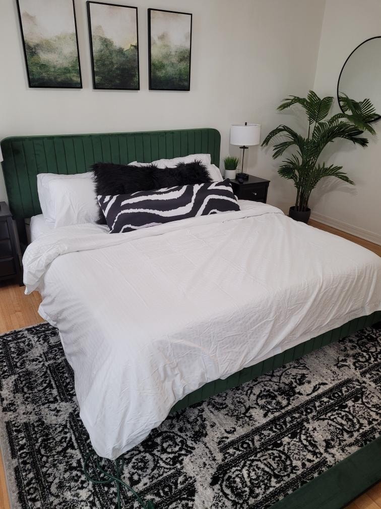 Green upholstered bed with white bedding, graphic pillow, and patterned rug