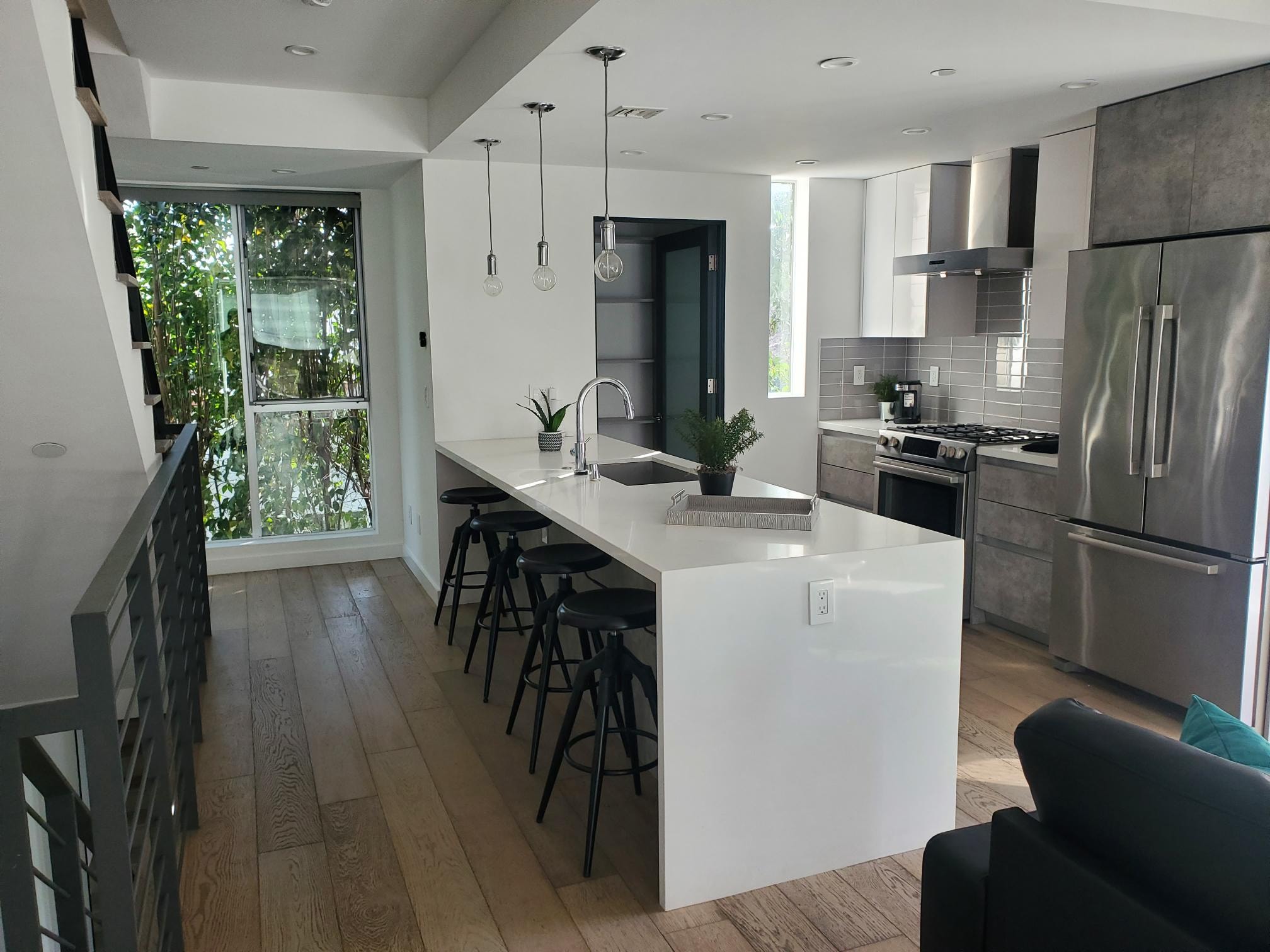 Modern white kitchen with waterfall island, black stools, and stainless steel appliances
