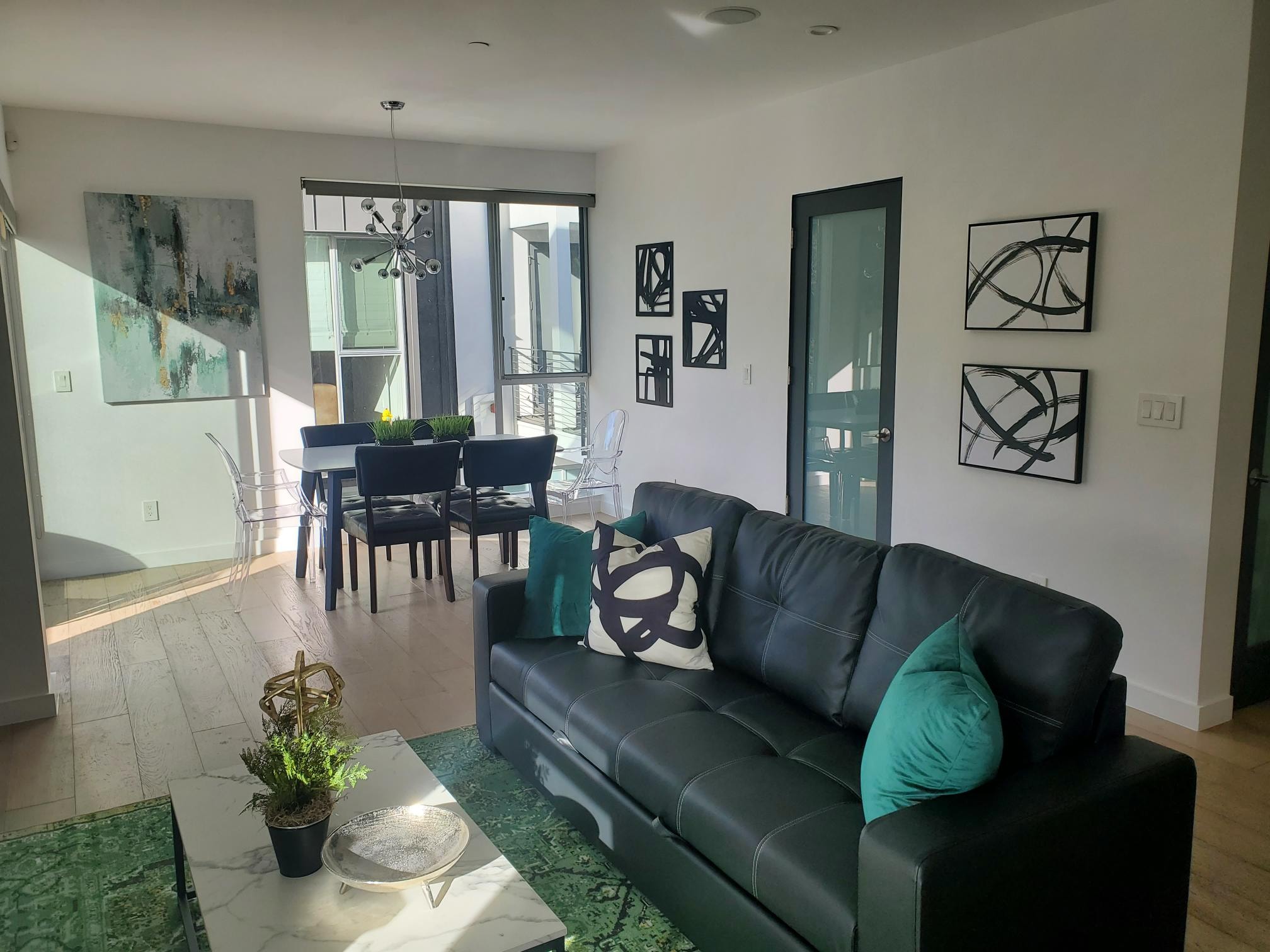 Charcoal leather sofa with teal pillows, graphic art, and dining area