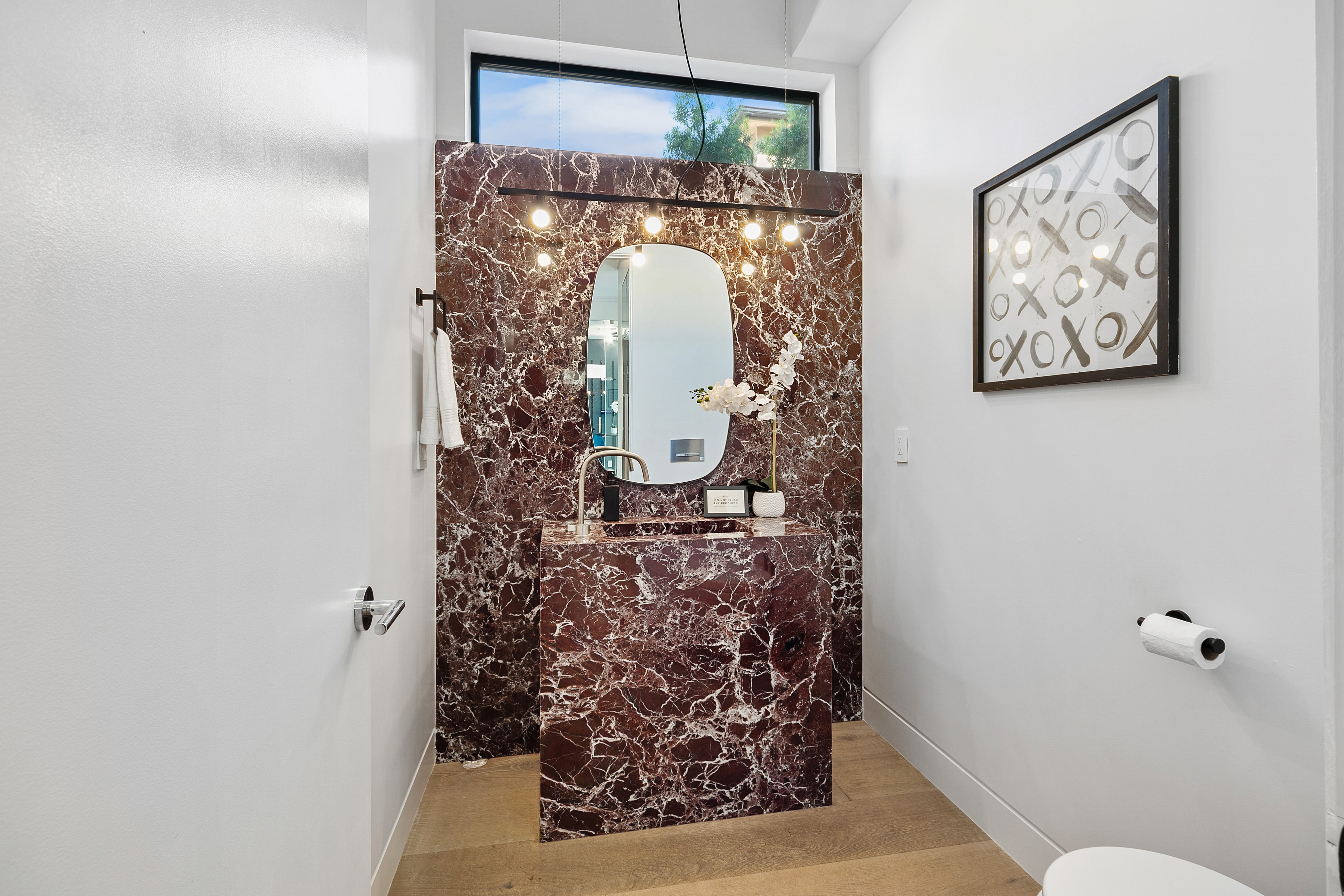 Dramatic burgundy marble powder room with sculptural mirror and warm lighting