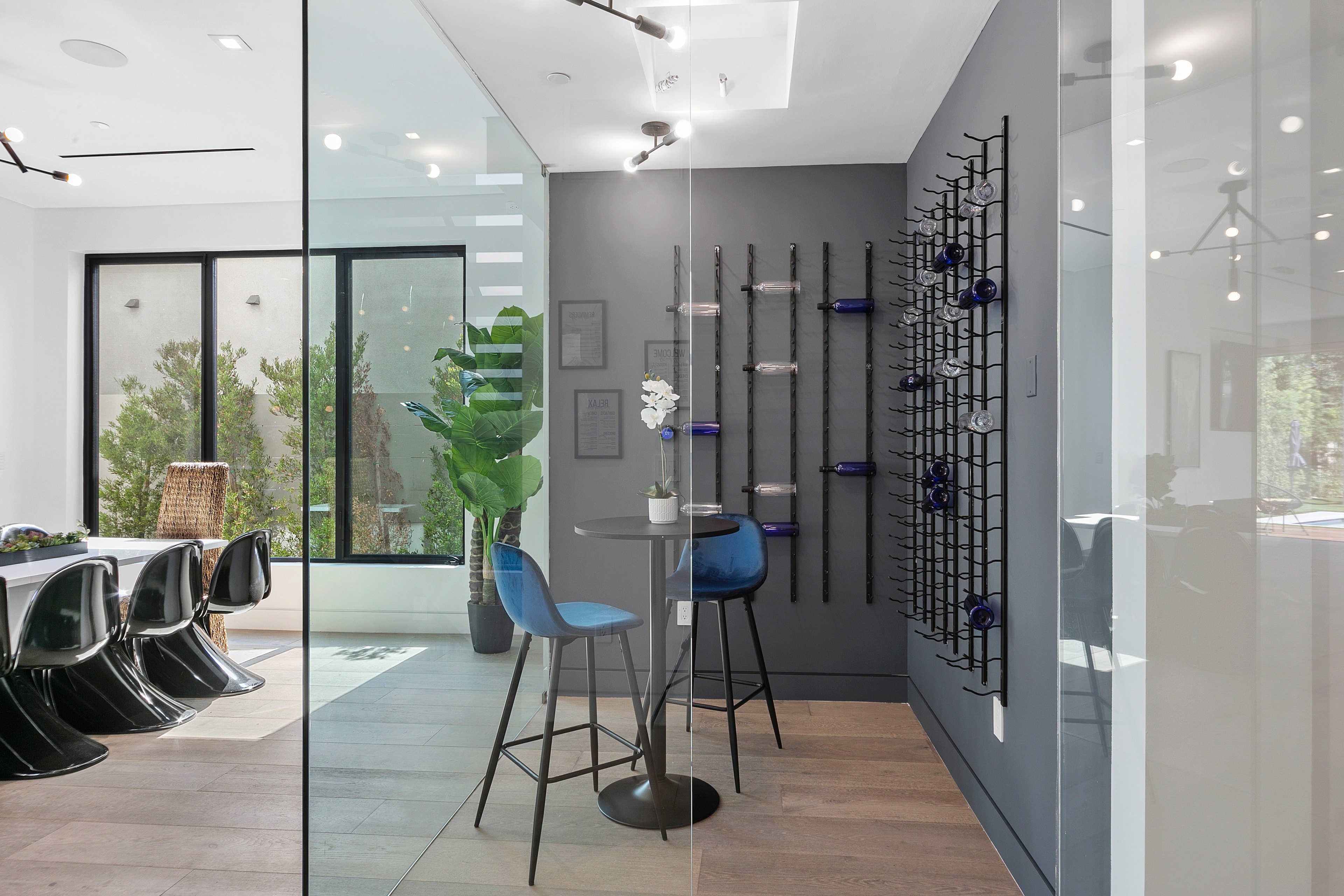 Glass-enclosed wine room with blue seating and modern dining area