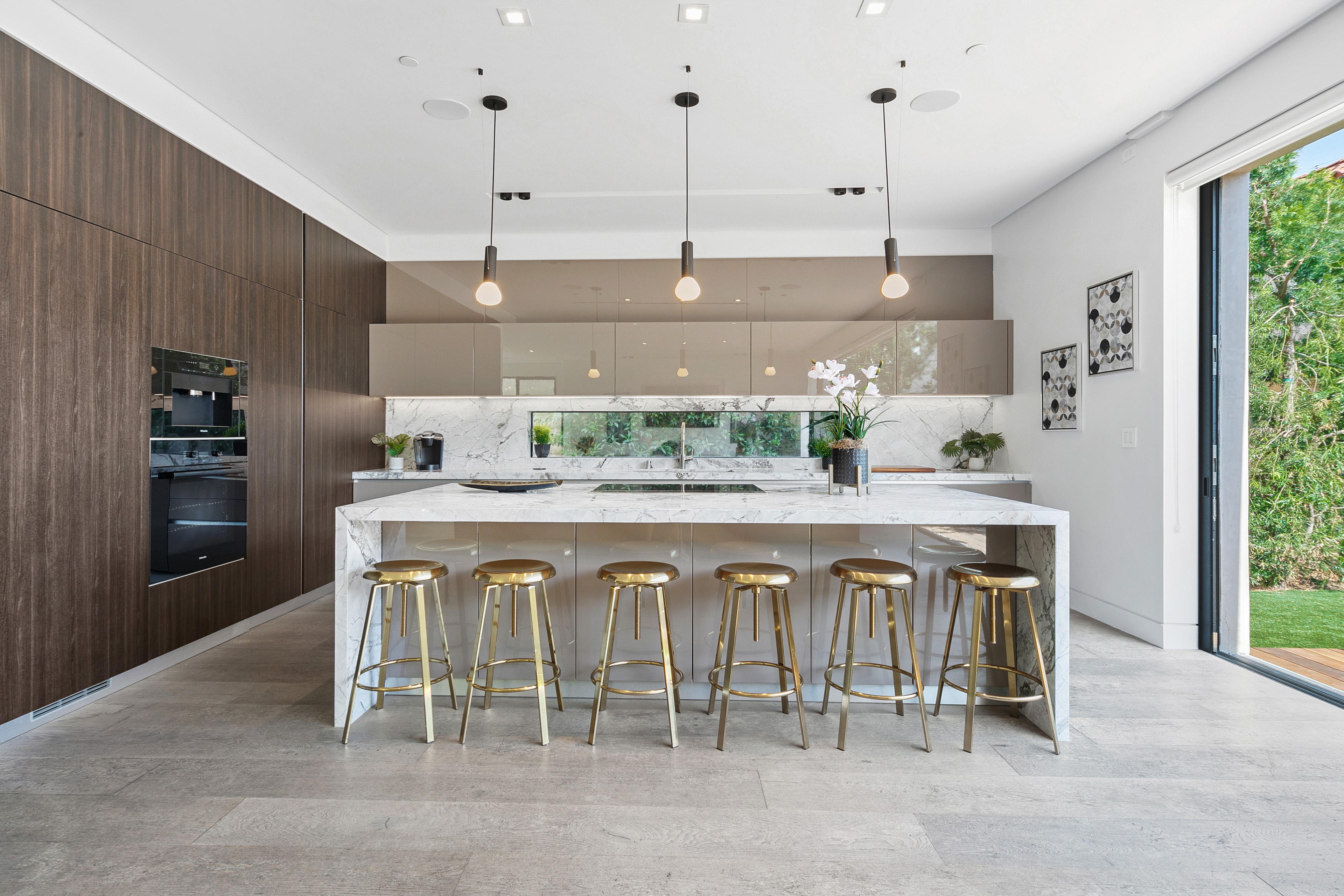 Contemporary kitchen with marble island, brass stools, and dark wood cabinetry