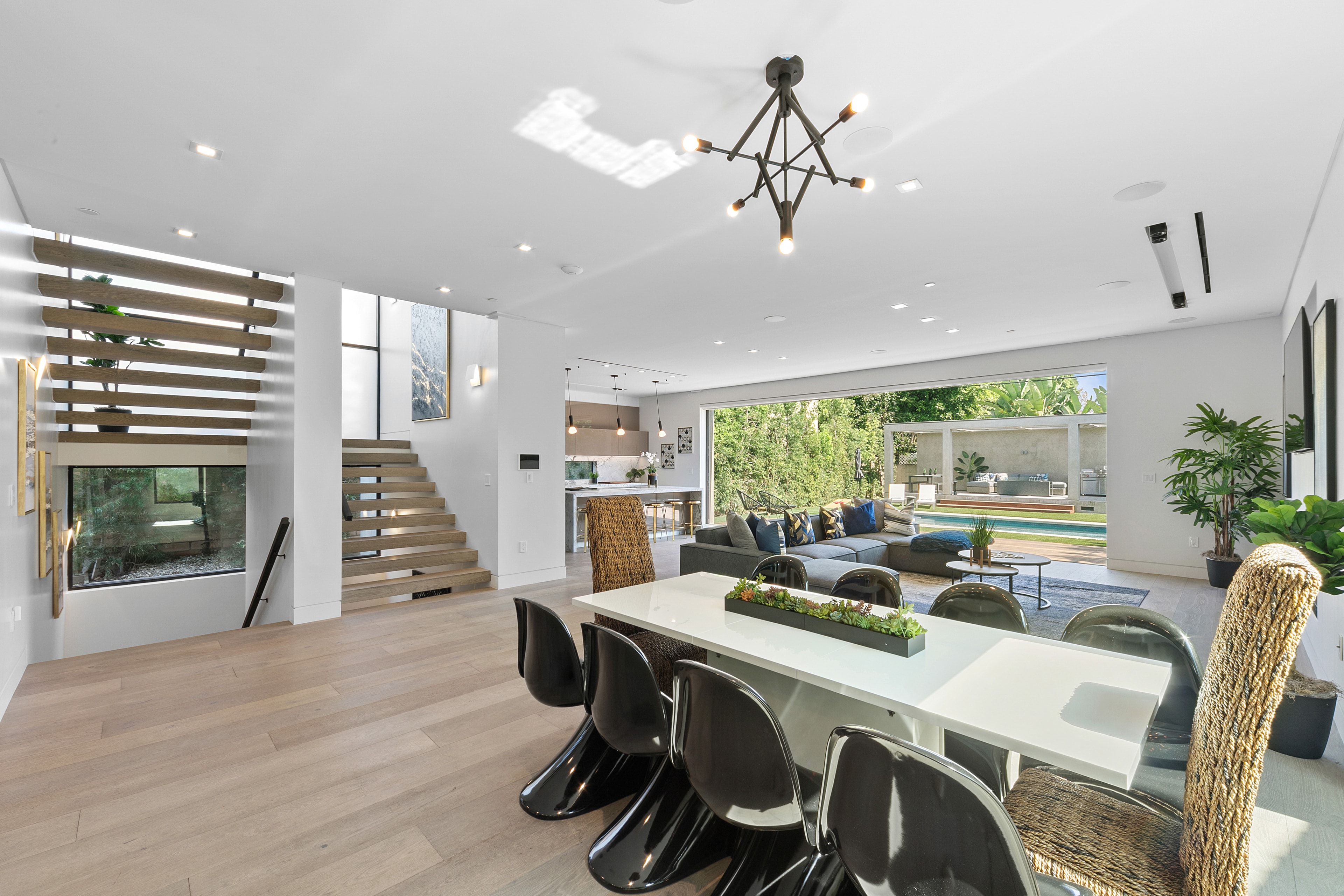 Open-plan dining and living area with staircase, kitchen, and pool view in daylight