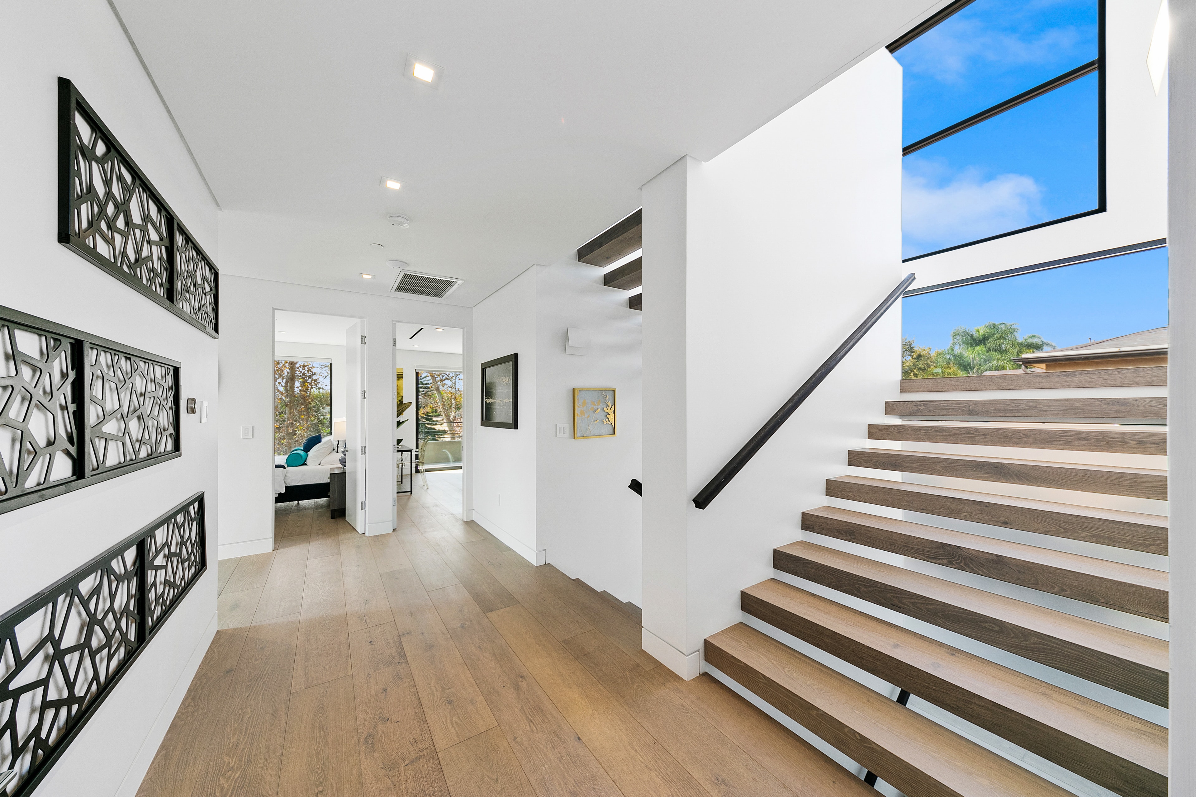 Second-floor hallway with floating wood staircase, black wall art, and tall windows