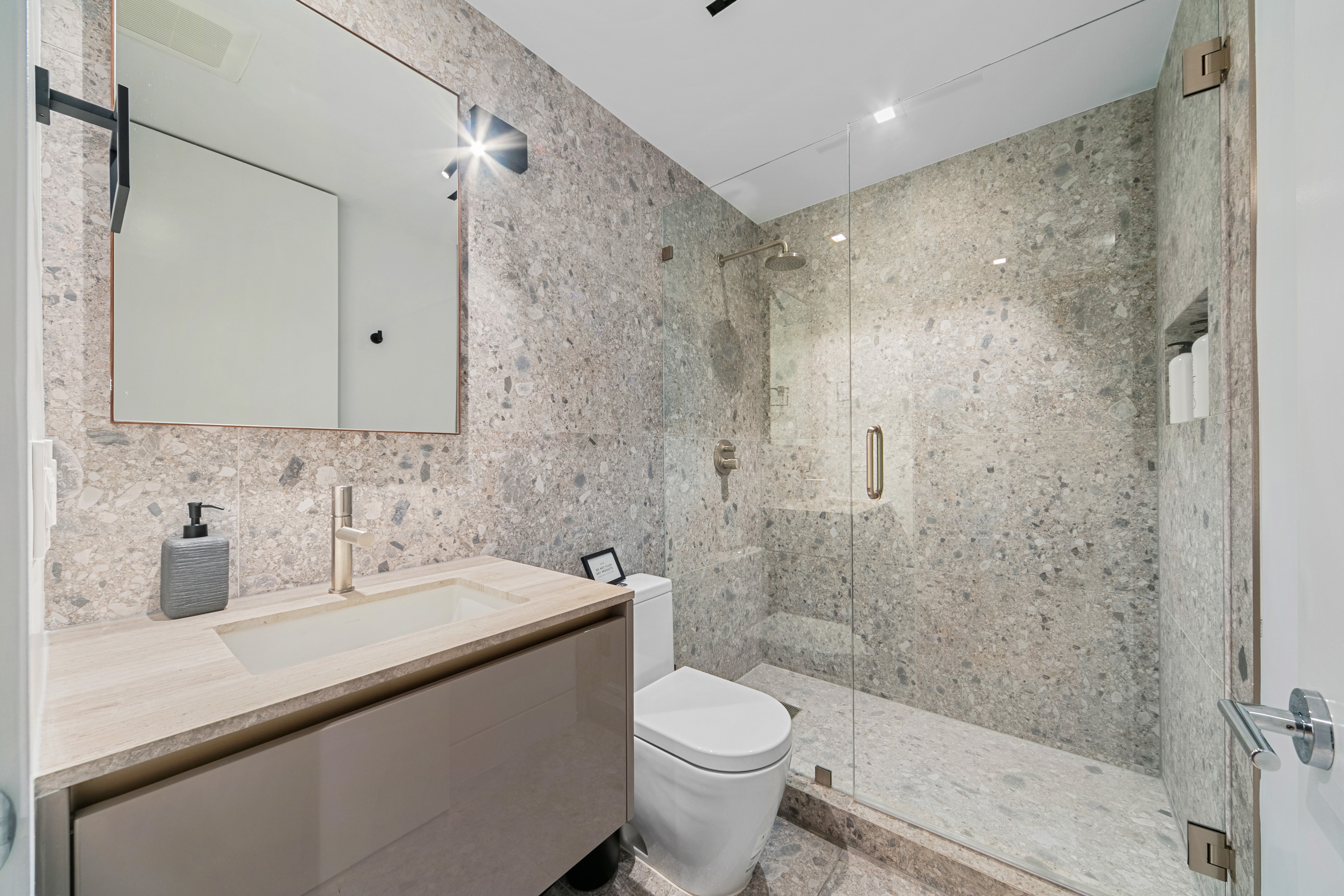 Stone-finished basement bathroom with glass shower and floating vanity