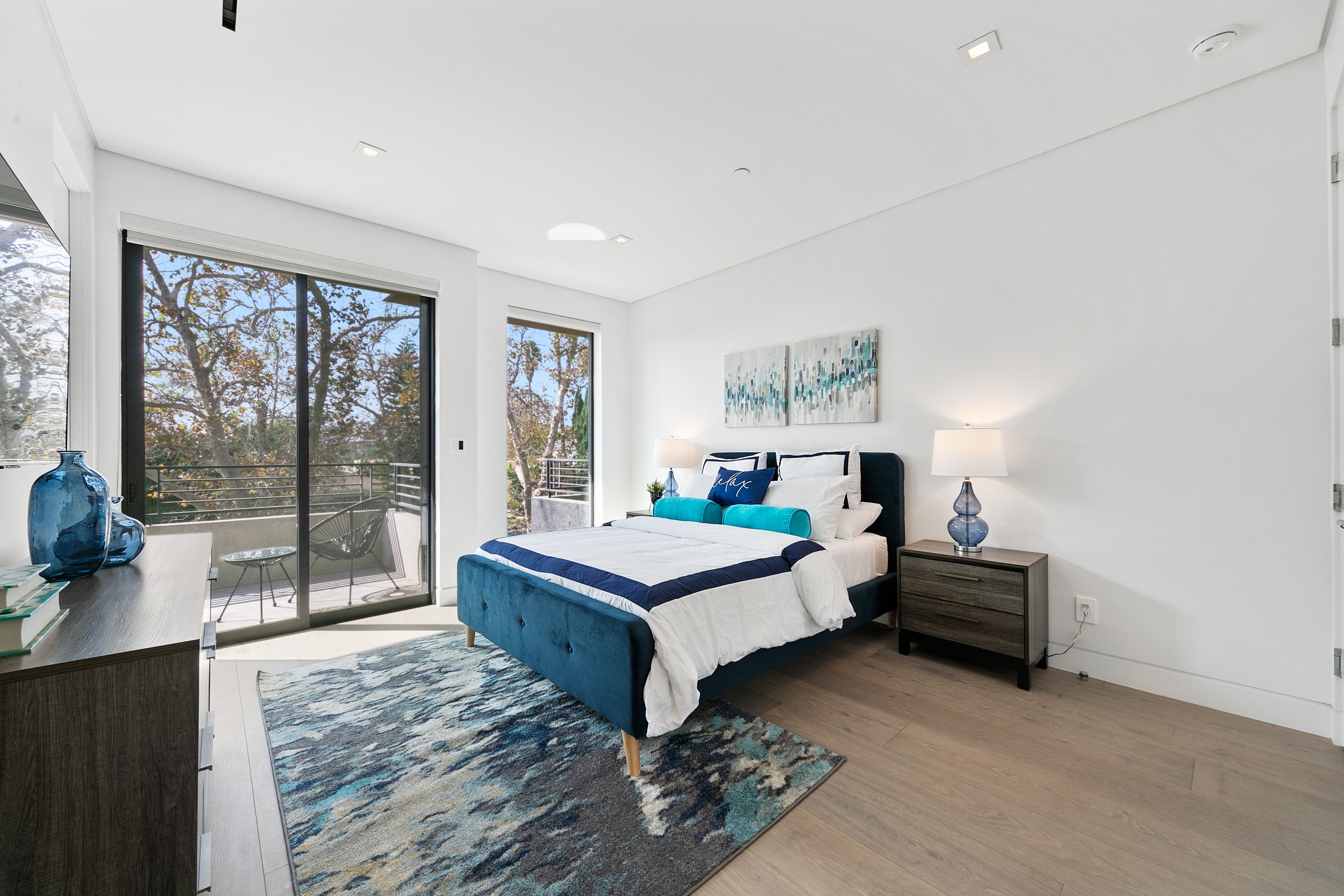 Upstairs bedroom with blue upholstered bed, balcony, and patterned rug