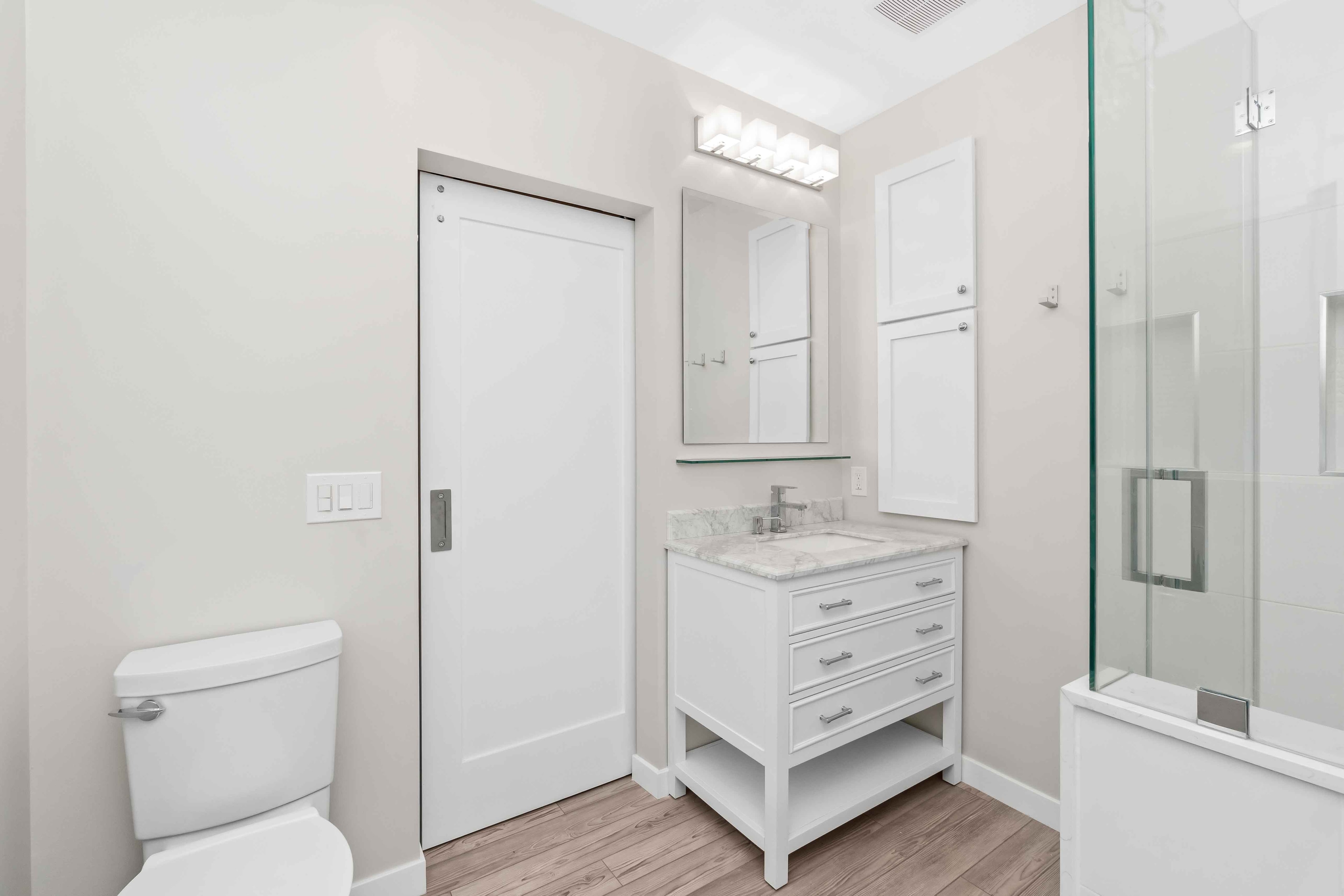 Remodeled bathroom with white vanity, marble countertop, and glass shower enclosure