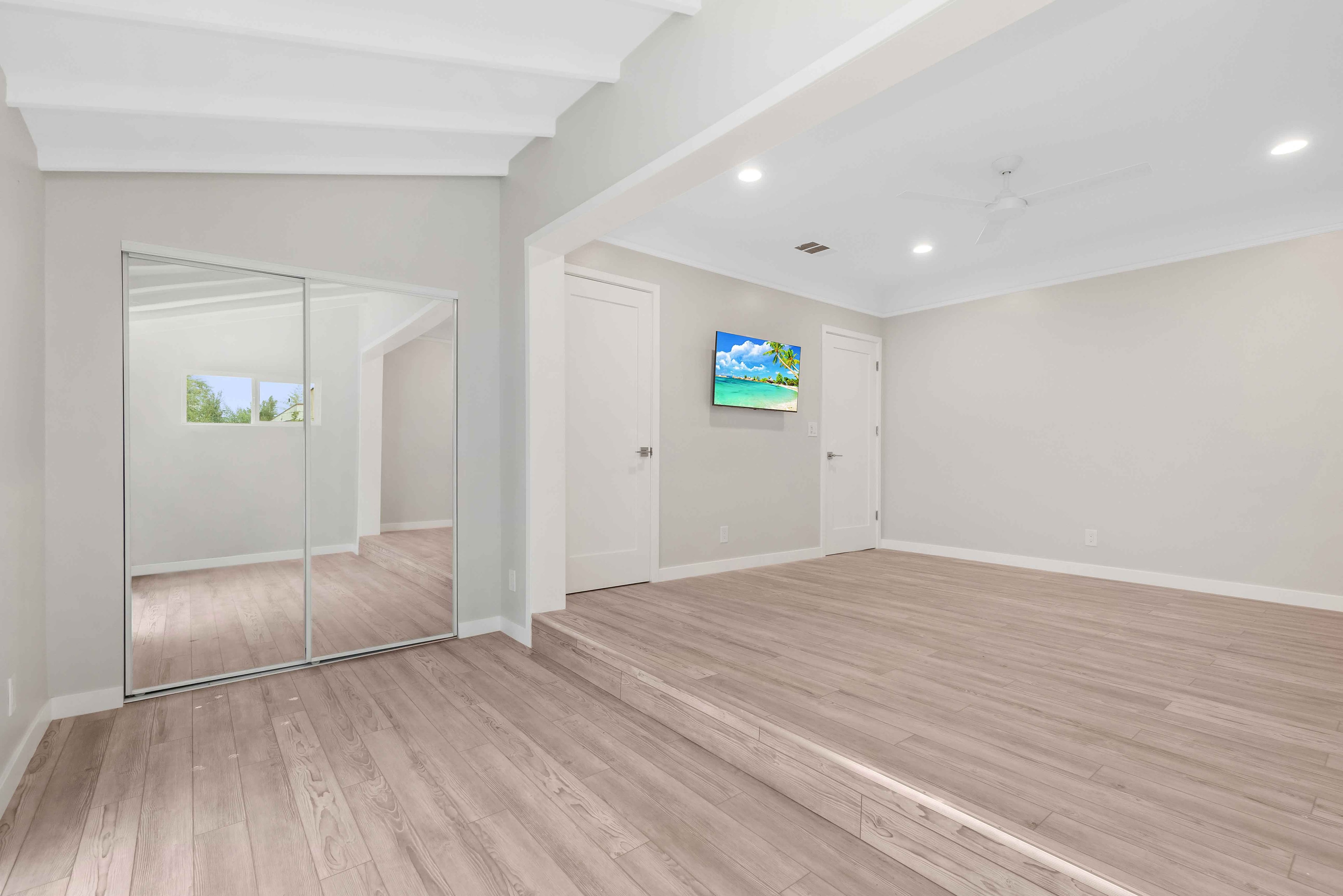 Bright remodeled bedroom with mirrored closet doors and light wood flooring