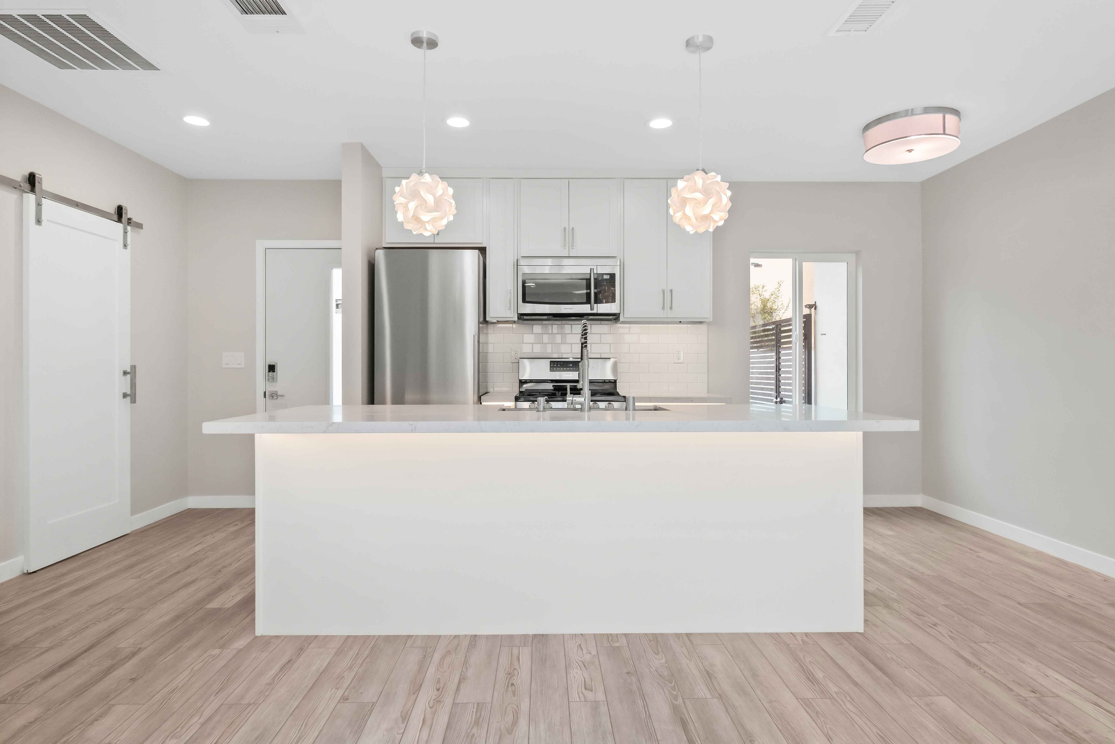 Front view of white kitchen island with stainless steel appliances and pendant lights