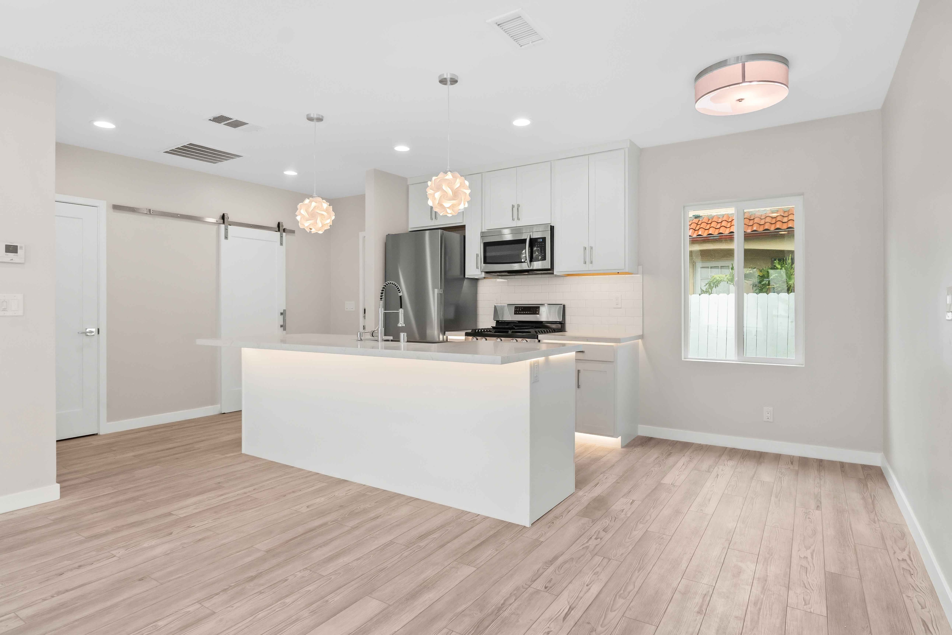 Wide view of remodeled white kitchen with island and light wood flooring