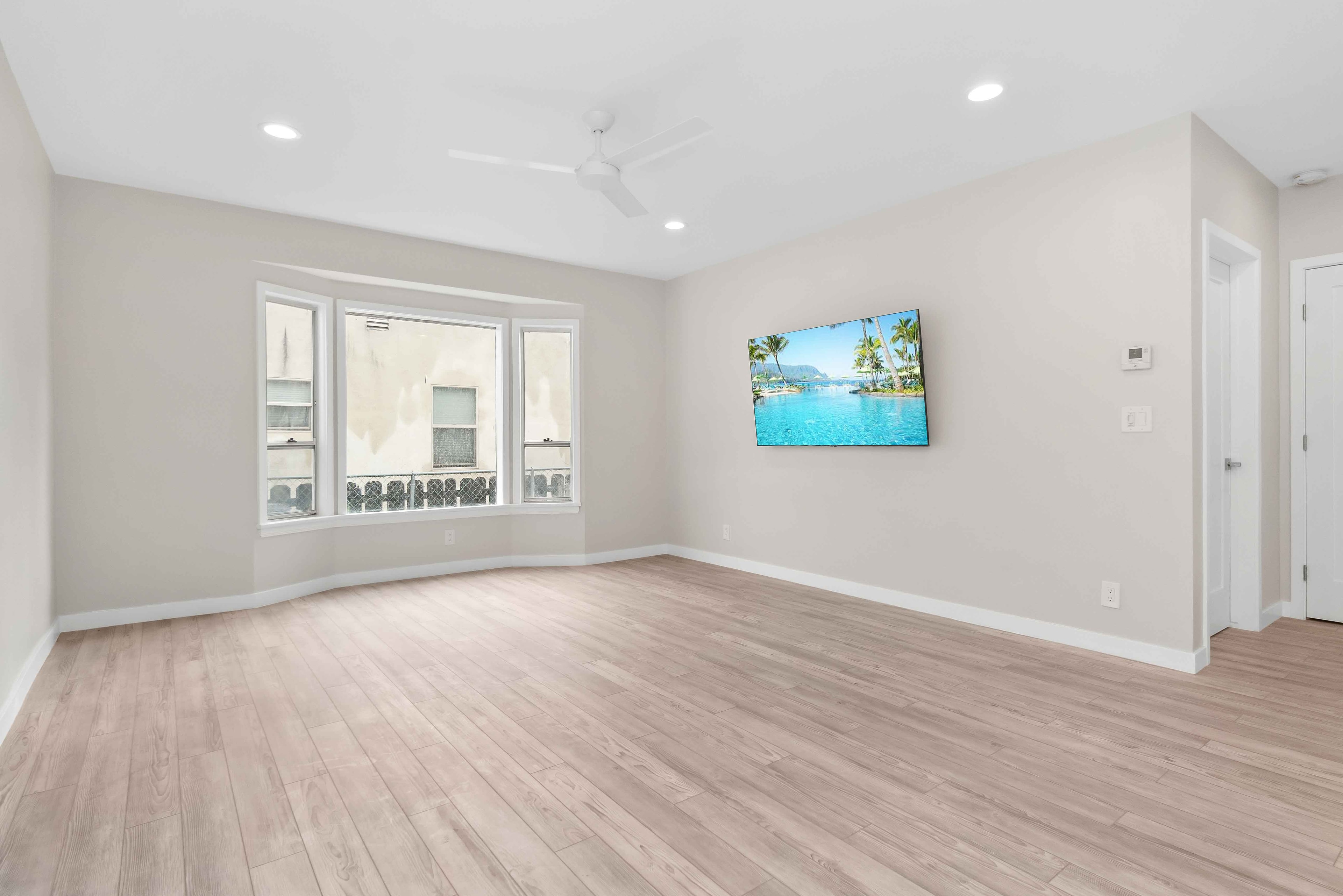 Bright remodeled living room with bay window, light wood flooring, and wall-mounted television