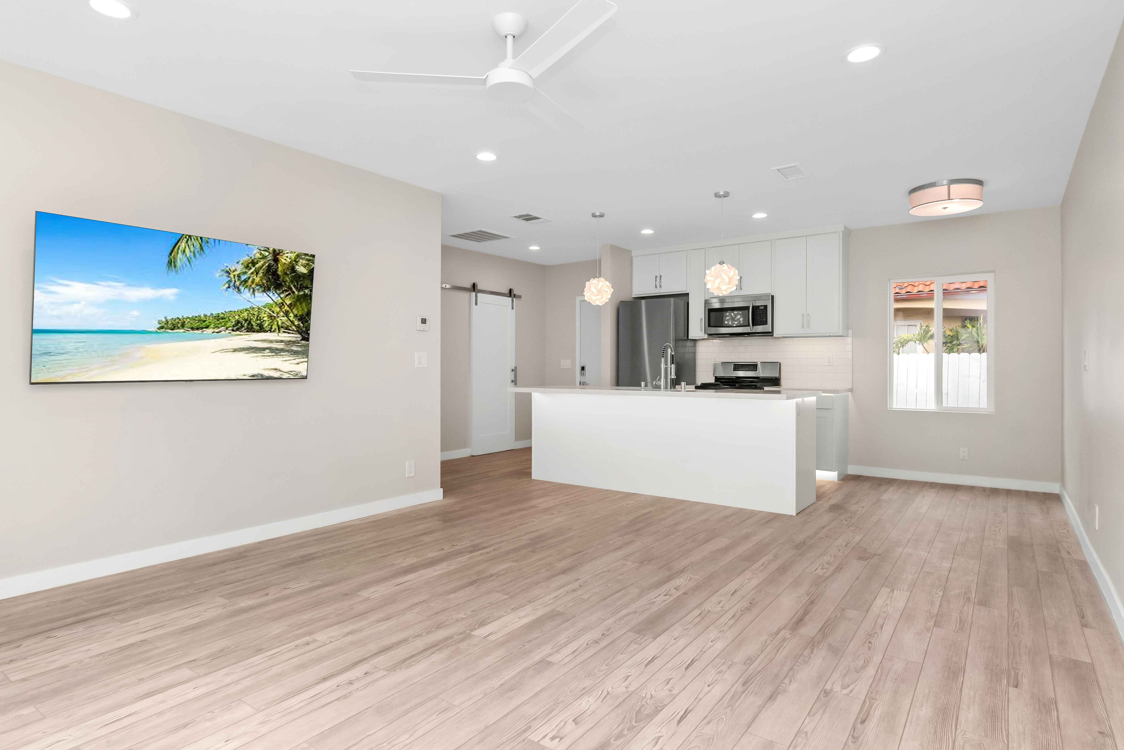 Open-plan living area and white kitchen with beach artwork and light wood flooring