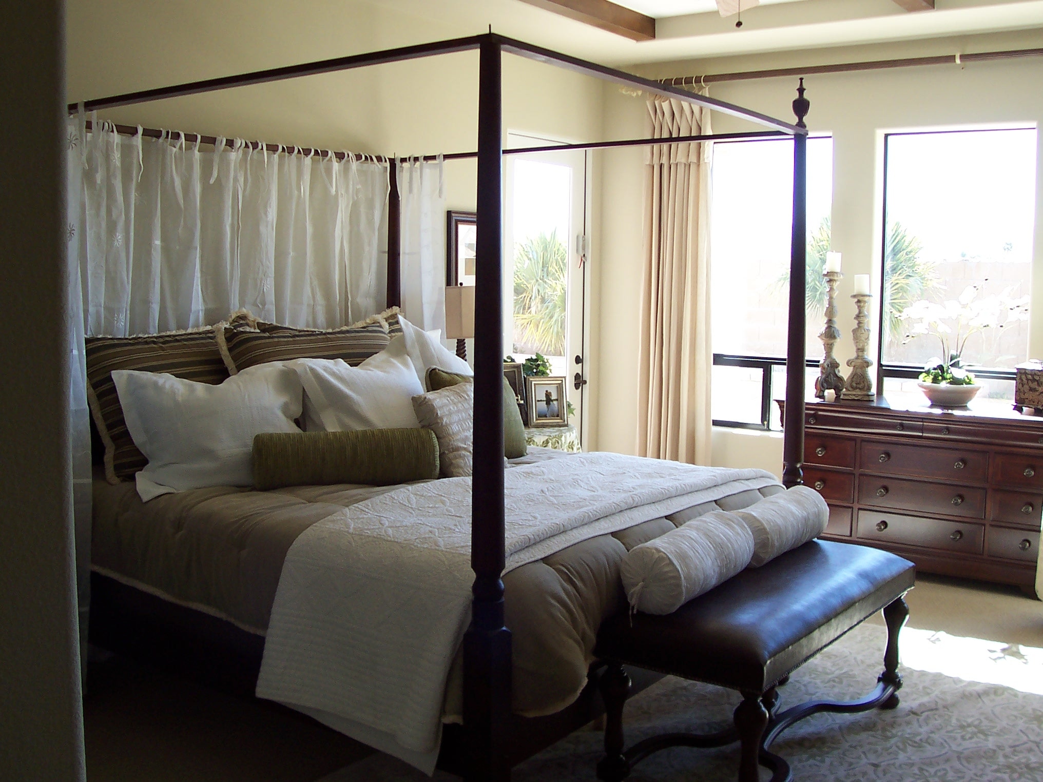 Bright four-poster bedroom with neutral bedding and dark wood furniture